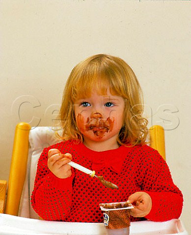 Toddler eating chocolate mousse sitting in her highchair