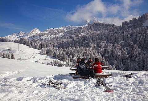 Snowboarders have lunch break by the Les Annes piste with Pointe Perce beyond at 2752m the highest peak in the Chaine des Aravis   Le GrandBornand HauteSavoie France