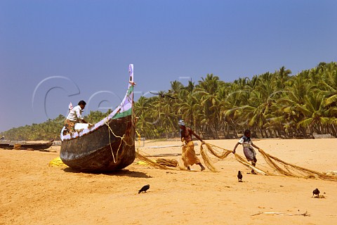 Fishermen busy with their nets and boat on the palm fringed beach north of Thiruvananthapuram Trivandrum Kerala India