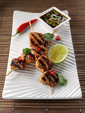 Two chicken kebabs on skewers with dipping sauce