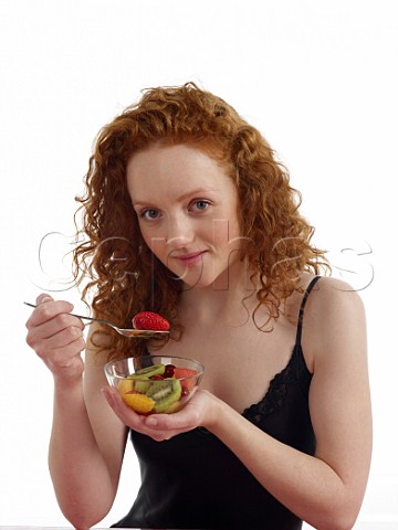 Young woman sitting at breakfast table with bowl of fresh fruit salad