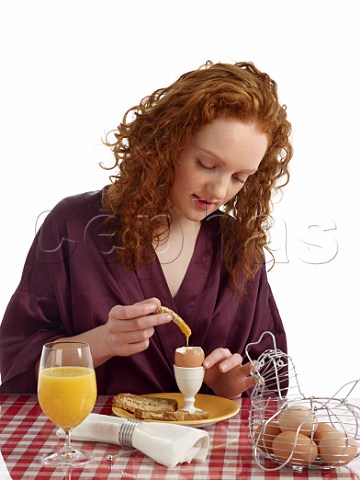 Young woman at breakfast table boiled eggs with brown bread soldiers glass of orange juice