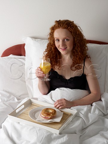 Young woman having breakfast in bed bagel with ham and cream cheese glass of orange juice