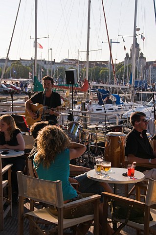 Busker playing to diners at one of many openair restaurants overlooking the ancient harbour at La Rochelle CharenteMaritime France