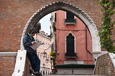 Man reading morning newspaper on canal bridge San Polo Venice Italy