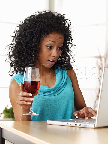 Young woman working with laptop computer while drinking wine