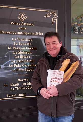 Man standing outside a Boulangerie with two baguettes that he has bought on Christmas Day Le PerreuxsurMarne near Paris France