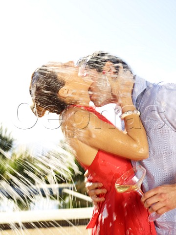 Couple celebrating whilst drinking champagne with champagne being sprayed over them