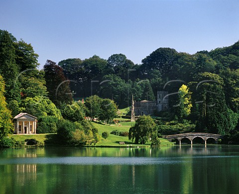 View over lake at Stourhead Gardens with Temple of Flora Bristol Cross StPeters Church and Turf Bridge Stourhead Wiltshire England