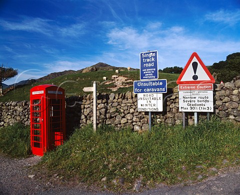 Red telephone box and road warning signs at foot of   Hardknott Pass in the Lake District Cumbria England