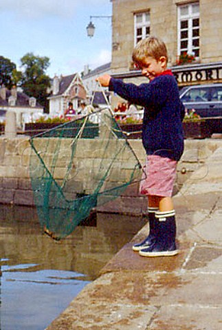 Five year old boy throwing net into  harbour to catch crabs StGoustan  Brittany France