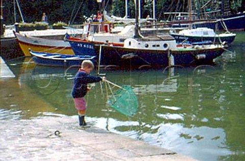 Five year old boy throwing net into  harbour to catch crabs StGoustan  Brittany France