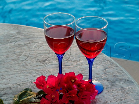 Red wine glasses  sprig of Bougainvillea on   poolside table