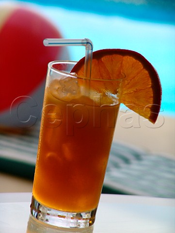 Glass of iced orange juice with pool  beach ball   behind  Florida USA