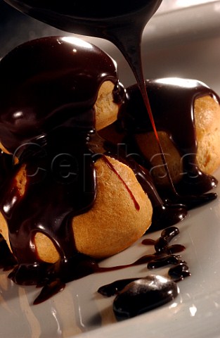 Profiteroles being covered in dark chocolate