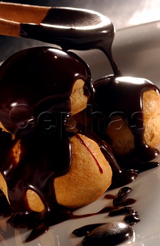 Profiteroles being covered in dark chocolate