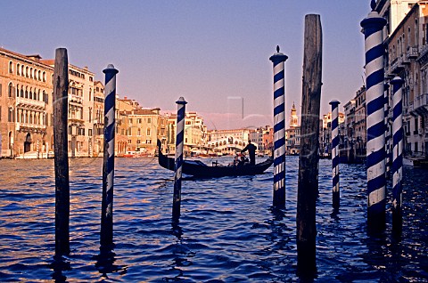 Gondola silhouetted against the Rialto Bridge in   late afternoon sun viewed through mooring posts   Venice Italy