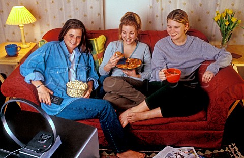 Three girl flatmates enjoy a relaxed TV snack of   popcorn and pizza