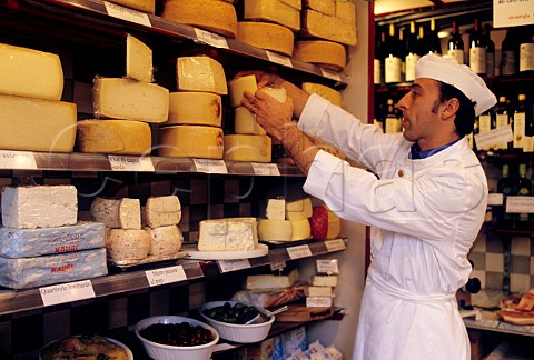 Shopkeeper in Italian delicatessen setting out his  display of cheeses Siena Tuscany Italy