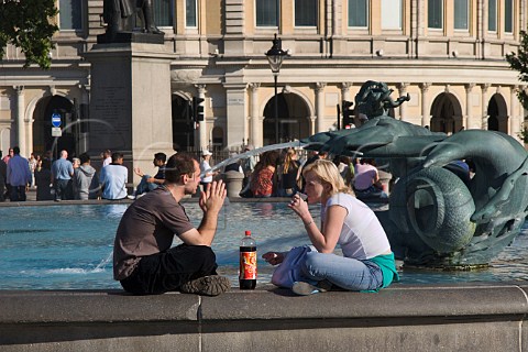 Couple relaxing next to the fountains in Trafalgar   Square London
