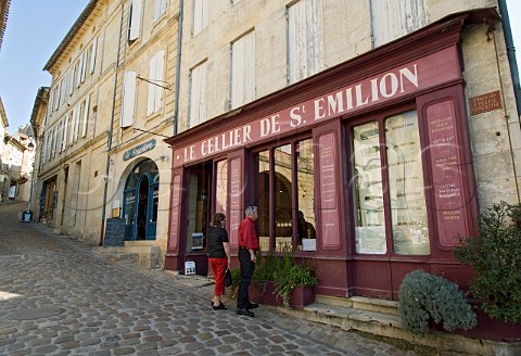 Tourist couple look in the windows of Le Cellier de   Stmilion wine shop in the cobbled central  square   of Saintmilion Gironde France