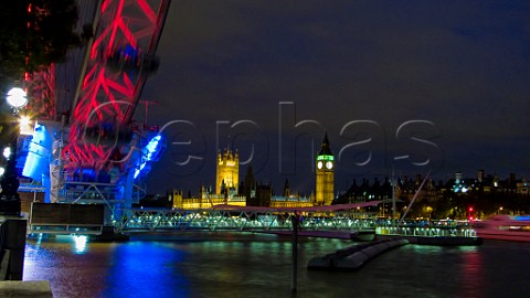 The Houses of Parliament across the River Thames at night with the London Eye observation wheel in the foreground London England