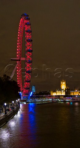 The Houses of Parliament across the River Thames at night with the London Eye observation wheel in the foreground London England