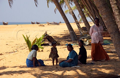 Family sheltering in the shade of the morning sunshine on the palm fringed beach north of Thiruvananthapuram Trivandrum Kerala India