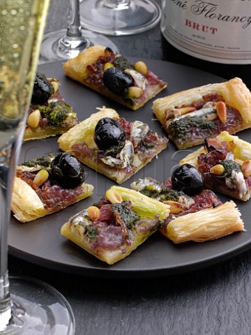 Pieces of pissaladiere on a black plate with champagne glass and bottle