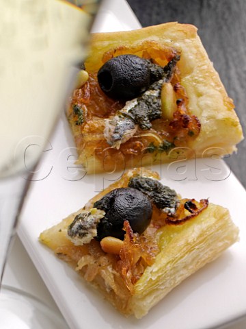 Two pieces of pissaladire pizza with black olives anchovies and pine nuts
