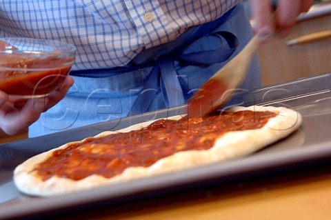 Spooning the tomato sauce onto a pizza base