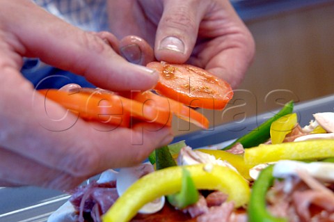 Adding sliced tomatoes peppers ham and salami to a pizza base