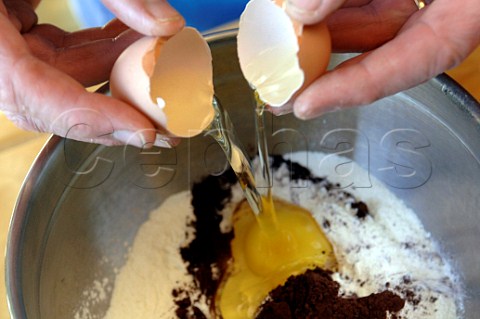 Cracking eggs into a mixing bowl with flour and cocoa for chocolate cake mix