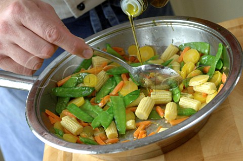 Pouring olive oil into bowl of fresh vegetables