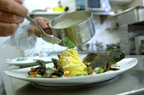 Chef spooning sauce over plate of tagliatelle and mussels