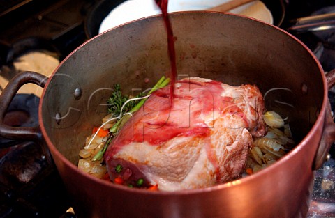 Pouring red wine into a saucepan to pot roast a joint of pork