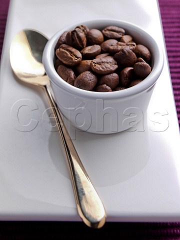 White ramekin full of coffee beans with a gold spoon