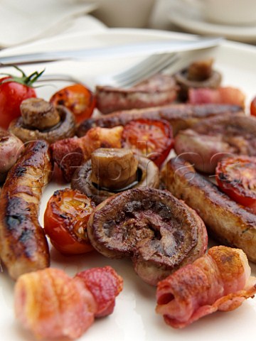 Mixed grill plate chipolata sausages kidneys mushrooms and grilled tomatoes in a table setting