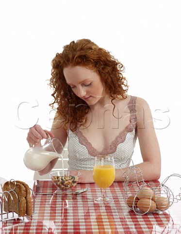 Young woman sitting at breakfast table fuit and nut muesli with milk wholemeal toast boiled eggs orange juice