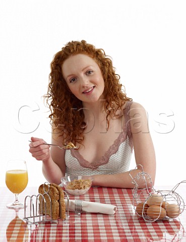 Young woman sitting at breakfast table Special K with milk wholemeal toast boiled eggs orange juice