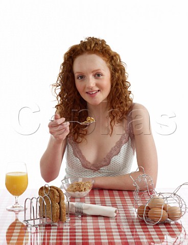 Young woman sitting at breakfast table Special K with milk wholemeal toast boiled eggs orange juice