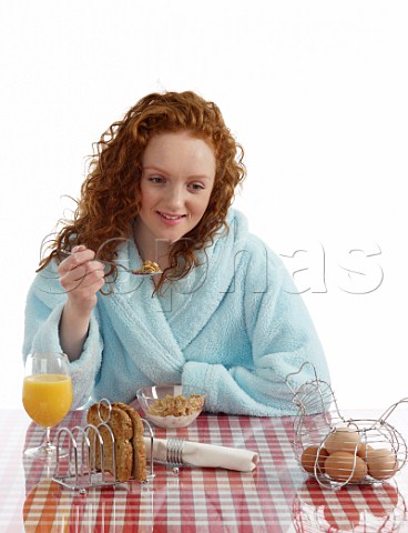 Young woman sitting at breakfast table Special K with milk wholemeal toast boiled eggs orange juice