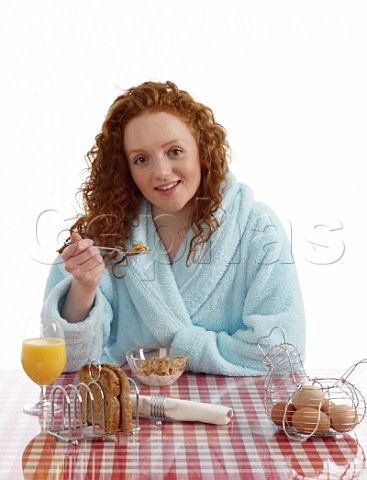 Young woman sitting at breakfast table Special K with milk wholemeal toast boiled eggs orange juice