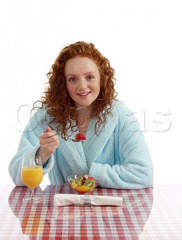 Young woman sitting at breakfast table fresh fruit salad and orange juice