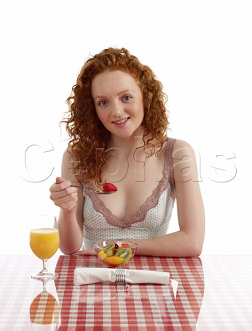 Young woman sitting at breakfast table fresh fruit salad and orange juice