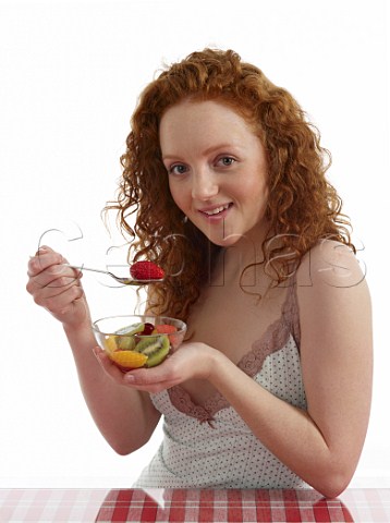 Young woman sitting at breakfast table with bowl of fresh fruit salad