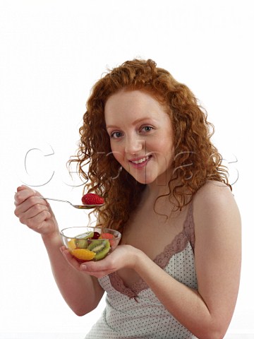 Young woman sitting at breakfast table with bowl of fresh fruit salad