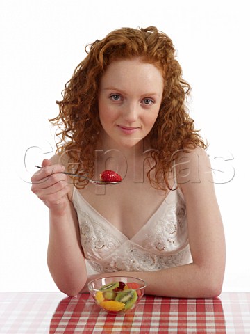 Young woman sitting at breakfast table with bowl of fresh fruit salad