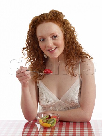 Young woman sitting at breakfast table with bowl of fresh fruit salad