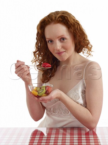 Young woman sitting at breakfast table with bowl of fresh fruit salad